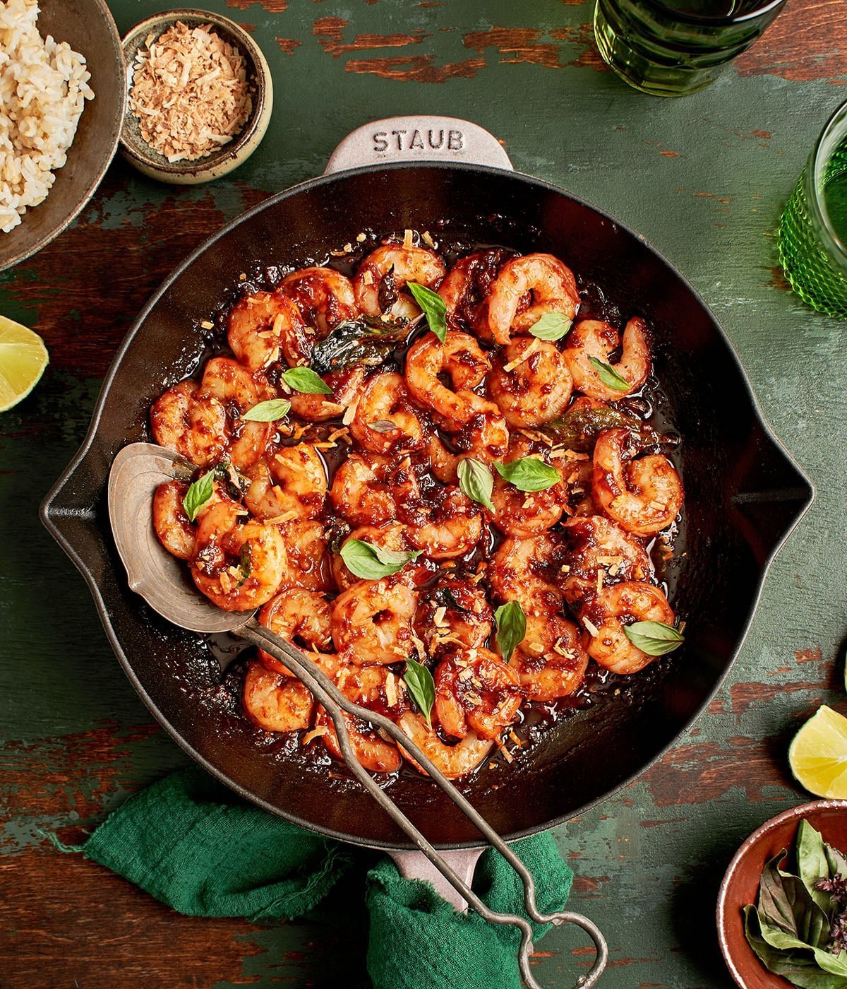 Petite poêle en fonte avec des crevettes sautées au piment et basilic, garnies de feuilles vertes, sur plan de bois, accompagnées de riz et lime. Effets du piment fort sur la santé.